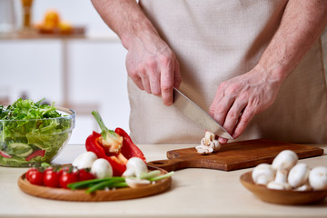 Man cooking at kitchen making healthy vegetable salad, close-up, selective focus.