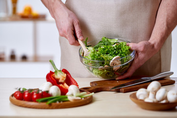 Man cooking at kitchen making healthy vegetable salad, close-up, selective focus.