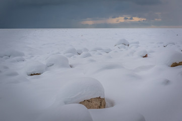 Rocks covered with snow. Dark clouds and frozen Baltic sea. Snowstorm.
