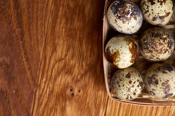 Quail eggs in a box on a rustic wooden background, top view, selective focus.