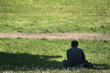 Naklejka na ściany i meble lonely man sitting on grass, back view of a person at the park 