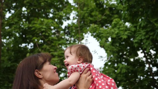 Young mom and baby laughing together while playing outdoors. Girl is jumping in air at hands of parent and smiling. Happy childhood. Slow motion.
