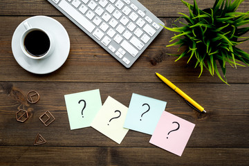 Question mark on sticky notes on office desk on dark wooden background top view. FAQ concept. Working with clients. Troubles in work.
