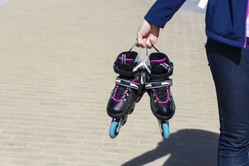 Closeup of a girl holding a roller skate. On the background of paving slabs.