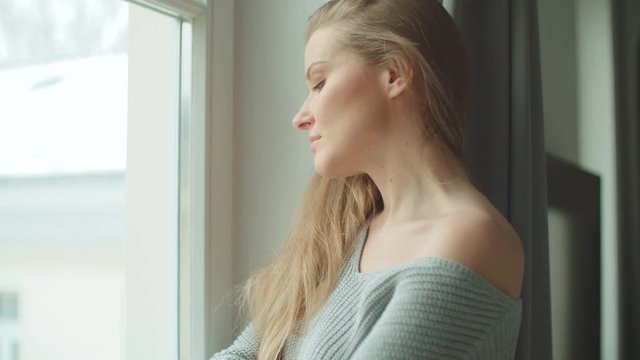 Young pensive woman standing by a window.
