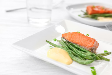 Plate with tasty fish and green beans on table