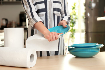 Woman wiping ceramic plate with paper towel indoors