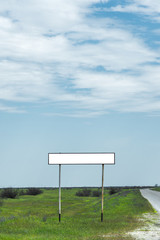 Empty old road sign for the name of a city or village populated area near the road in the countryside against a blue sky and white clouds surrounded by green grass