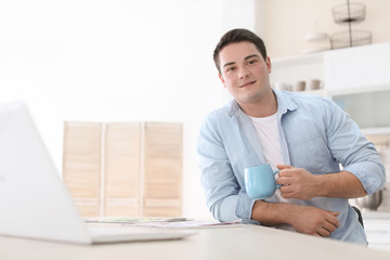 Portrait of confident young man with  laptop and cup at table
