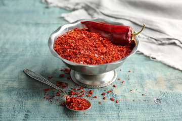 Bowl with crushed chili pepper and pod on wooden background