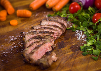 Juicy slices of grilled steak on wooden board