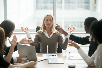 Female boss calming down meditating at stressful office meeting, peaceful mindful businesswoman practicing yoga ignoring avoiding multiracial employees at group meeting, no stress free relief concept