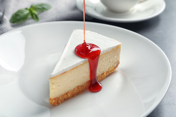 Pouring sweet jam onto delicious cheesecake served on plate