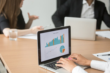 African businesswoman analyzing statistics on laptop screen at group meeting working with financial graphs charts online, business software for data analysis, project management concept, closeup view