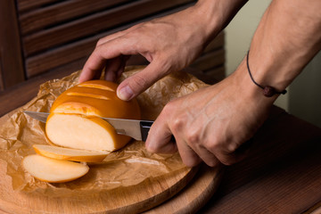 close up of men's hands  with a knife cut smoked homemade cheese