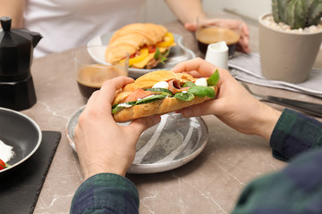 Man holding tasty croissant sandwich over plate at table