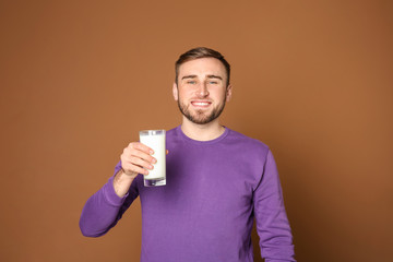 Young man with glass of tasty milk on color background