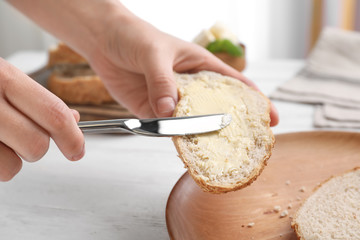 Woman spreading butter on slice of bread over table, closeup