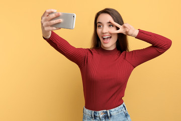 Attractive young woman taking selfie with phone on color background