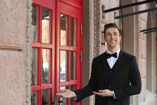 Young doorman in elegant suit standing near restaurant entrance