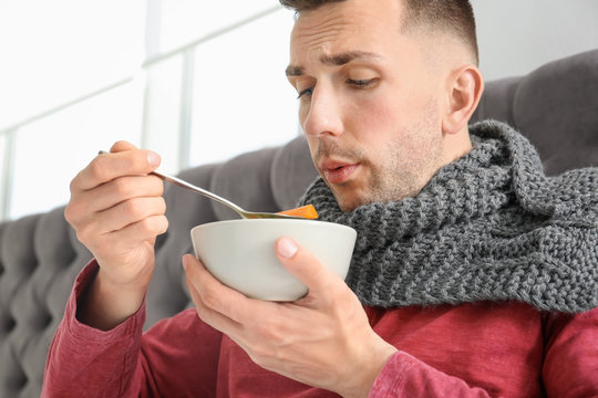 Sick young man eating broth to cure cold in bed at home