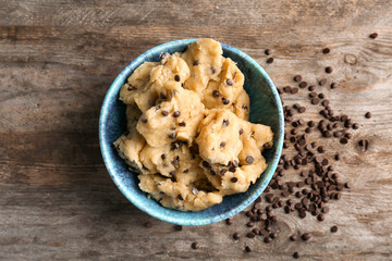 Raw cookie dough with chocolate chips in bowl on wooden background, top view