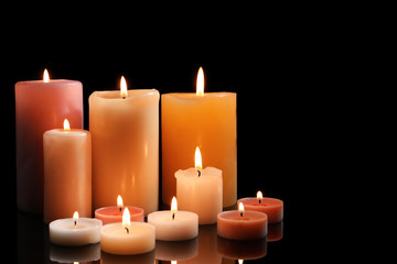 Fototapeta na wymiar Different wax candles burning on black background