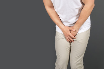 Young man with urological problems suffering from pain on grey background