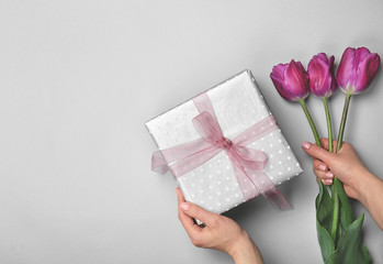Woman holding elegant gift box and tulips for Mother's Day on light background, top view