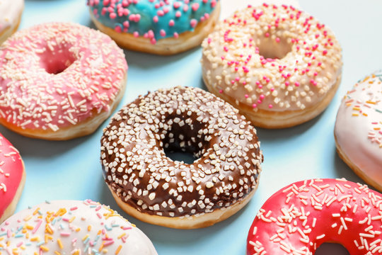 Delicious glazed doughnuts with sprinkles on color background