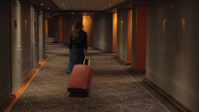 Steadicam shot of a woman with trolley case walking in hotel hallway to find the room and settle in