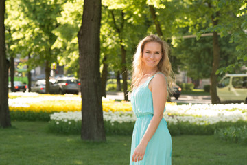 Waist up emotional portrait of the attractive blonde  woman in a blue dress on the street against the background of flowers