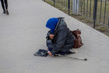 Old homeless woman is sitting on street and begging money 