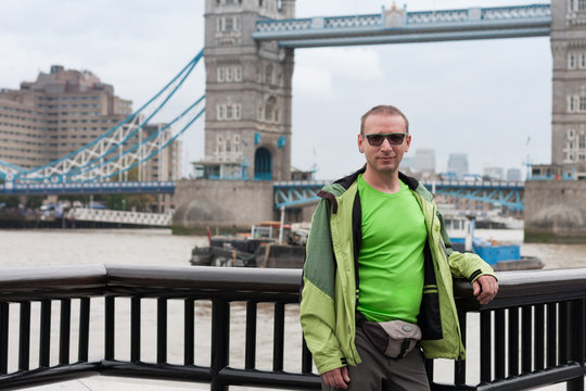 Caucasian man is standing on embankment of river Thames, on background Tower Bridge.
