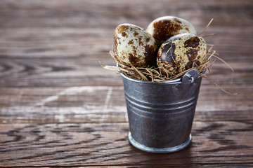 Small decorative bucket filled with quail eggs dark wooden table, close-up, selective focus.