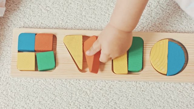 Child plays with wooden toy baby sorter with geometric figures. Top view