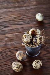 Fototapeta na wymiar Small decorative bucket filled with quail eggs dark wooden table, close-up, selective focus.