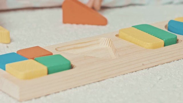 Child plays with wooden toy baby sorter with geometric figures