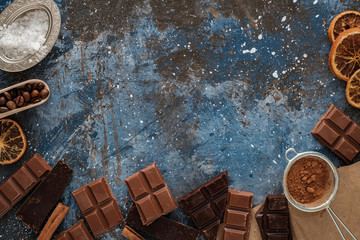 Dark and milk chocolate bars with dry orange slices, cinnamon sticks and coffee beans on blue...