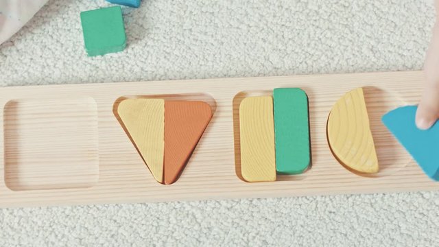 Child plays with wooden toy baby sorter with geometric figures. Top view. High speed