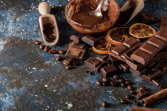 Dark and milk chocolate bars with dry orange slices, cinnamon sticks and coffee beans on blue background.