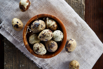 Rural still life with bowl full of eggs quail, eggs on a homespun napkin, boxwood on wooden background, top view