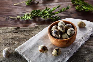 Rural still life with bowl full of eggs quail, eggs on a homespun napkin, boxwood on wooden background, top view