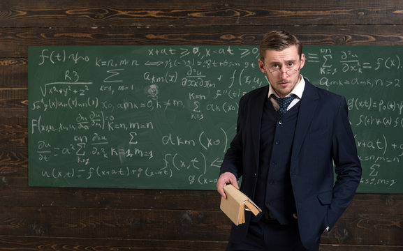 Anxious professor looking over his glasses. Intelligent man in suit holding book in classroom. Elite university concept