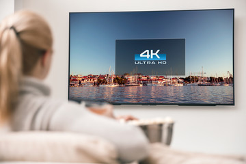 Naklejka premium Big modern TV with 4k resolutions and young woman on foreground watching some video