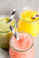 Detox organic diet drinks, homemade tropical smoothies - kiwi, orange, grapefruit, in portioned jars, on a gray stone table. Copy space