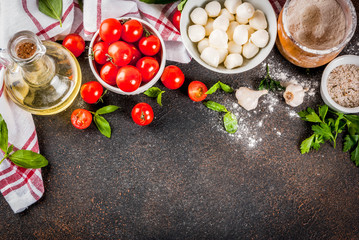 Homemade pasta pizza italian food ingredient on dark rusty table with flour, olive oil, basil, tomatoes and kitchen accessories top view