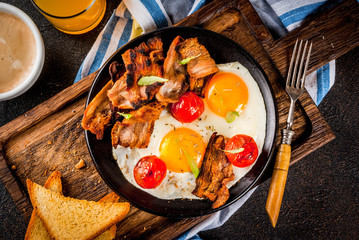 Traditional homemade english american breakfast, fried eggs, toasts, bacon, with coffee mug and orange juice dark background, top view copy space
