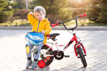 Happy kid boy of 3 years having fun in spring park with red bicycle on sunny day. Active child wearing bike helmet. Safety, sports, lifestyle, leisure with children