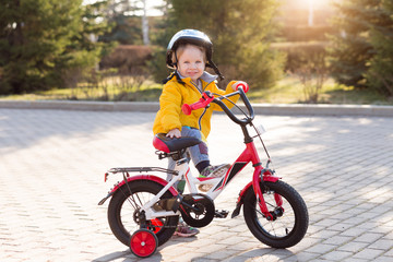 3 years old happy toddler boy riding red bike. Little kid learns to ride a bicycle. Sport, cycling, active playing, and childhood concept. First four-wheeled bike for little child.